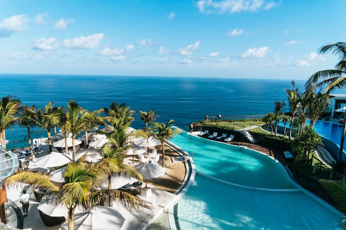 Des transats et des parasols autour d’une piscine d’hôtel bordée de palmiers